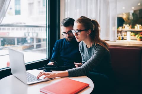 Couple in glasses looking at laptop in cafe